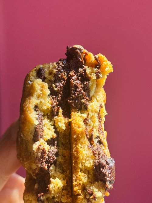Chocolate chip cookie held against a pink background