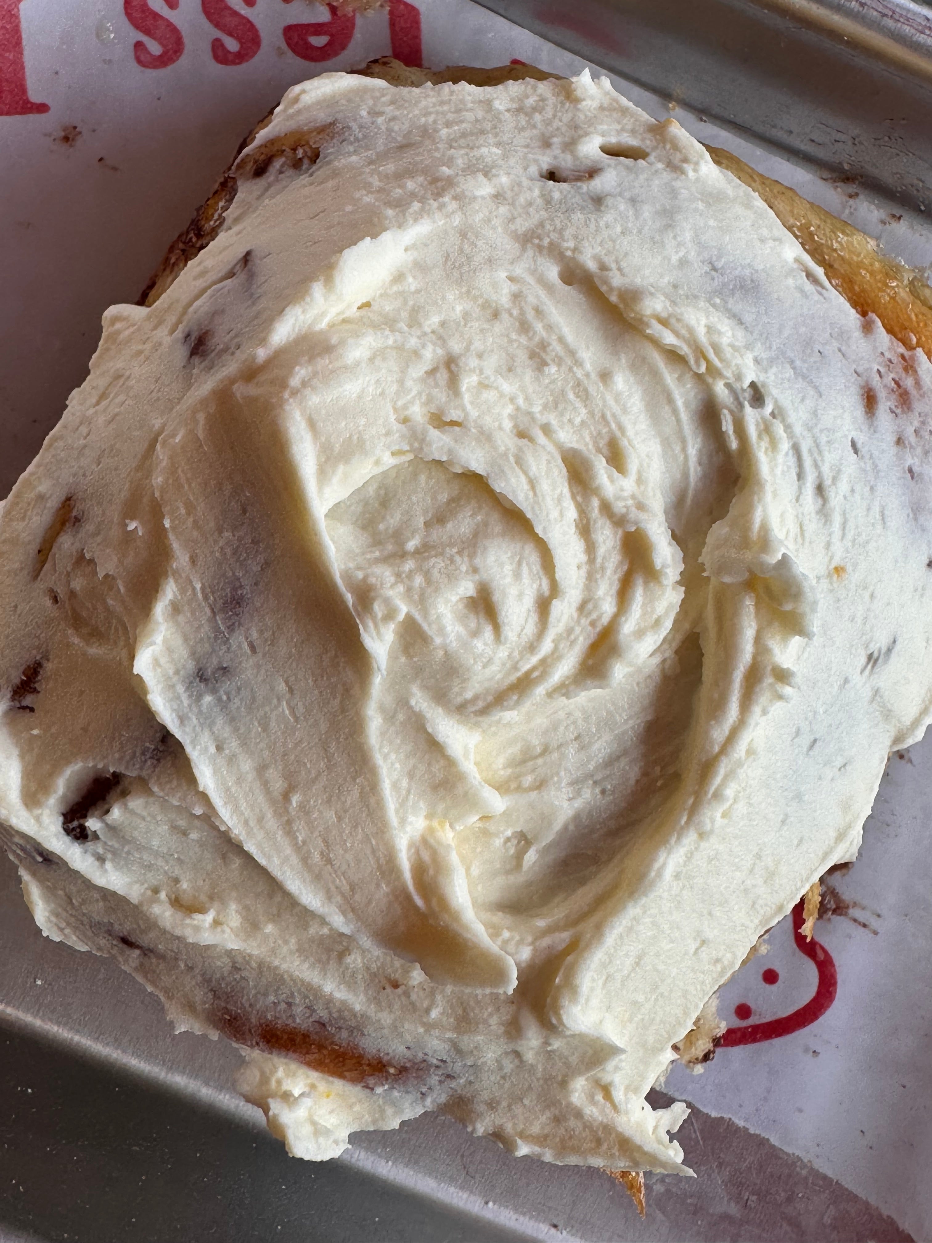 Close-up of a cinnamon roll with white frosting on a paper plate