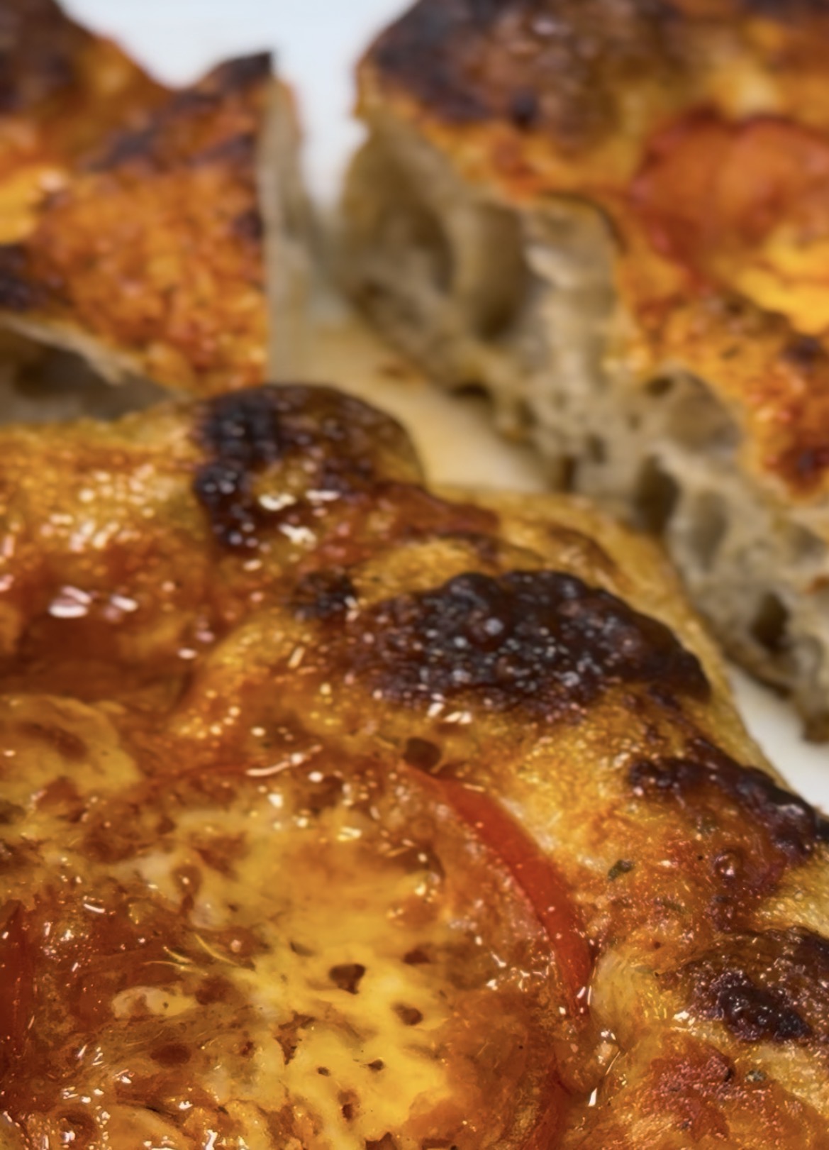 Close-up of a sourdough focaccia with charred crust, tomatoes and melted cheese