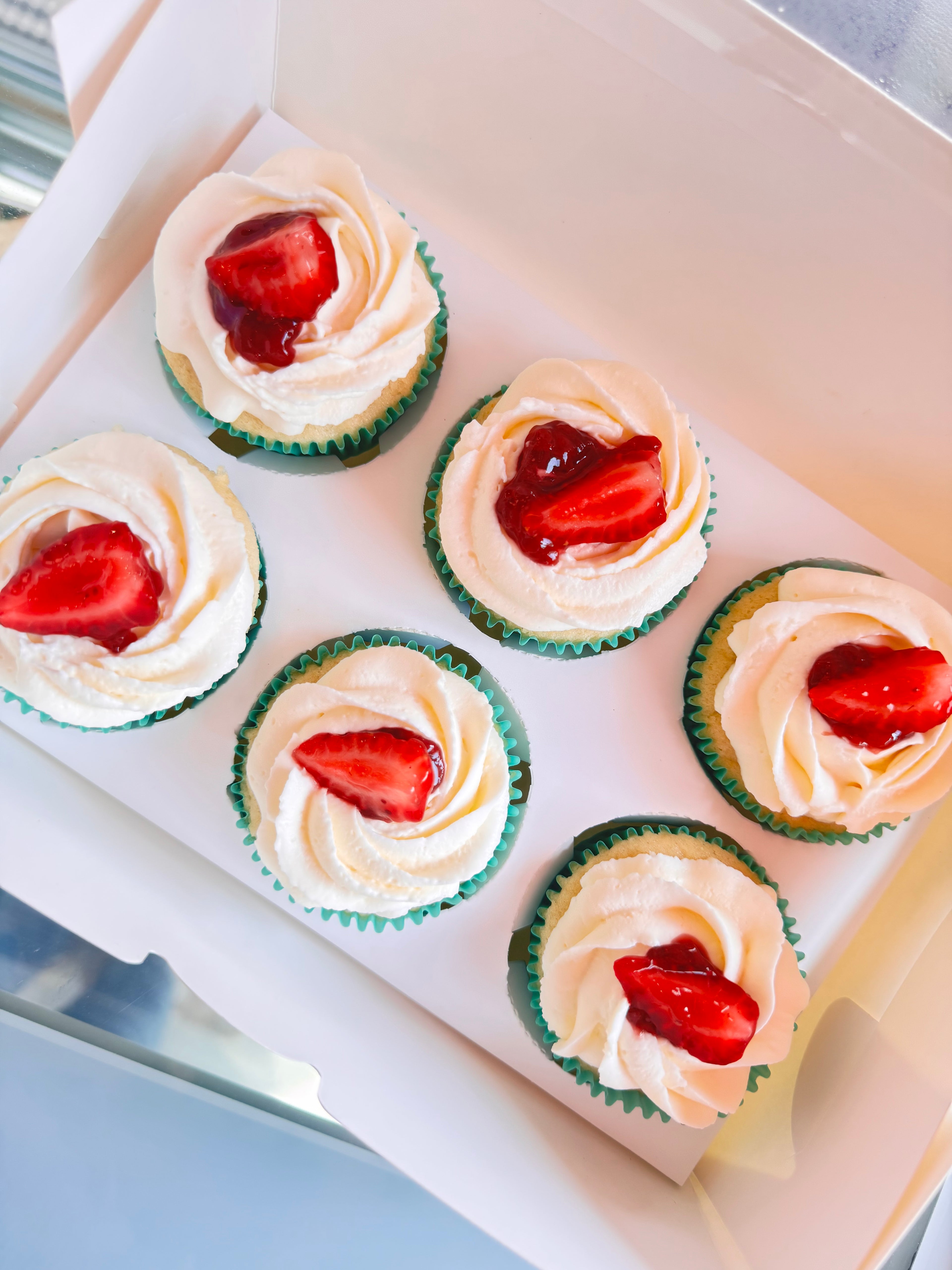 Cupcakes with white frosting and strawberry toppings on a tray.