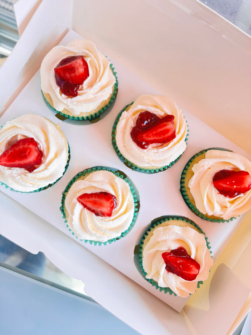 Cupcakes with white frosting and strawberry toppings on a tray.