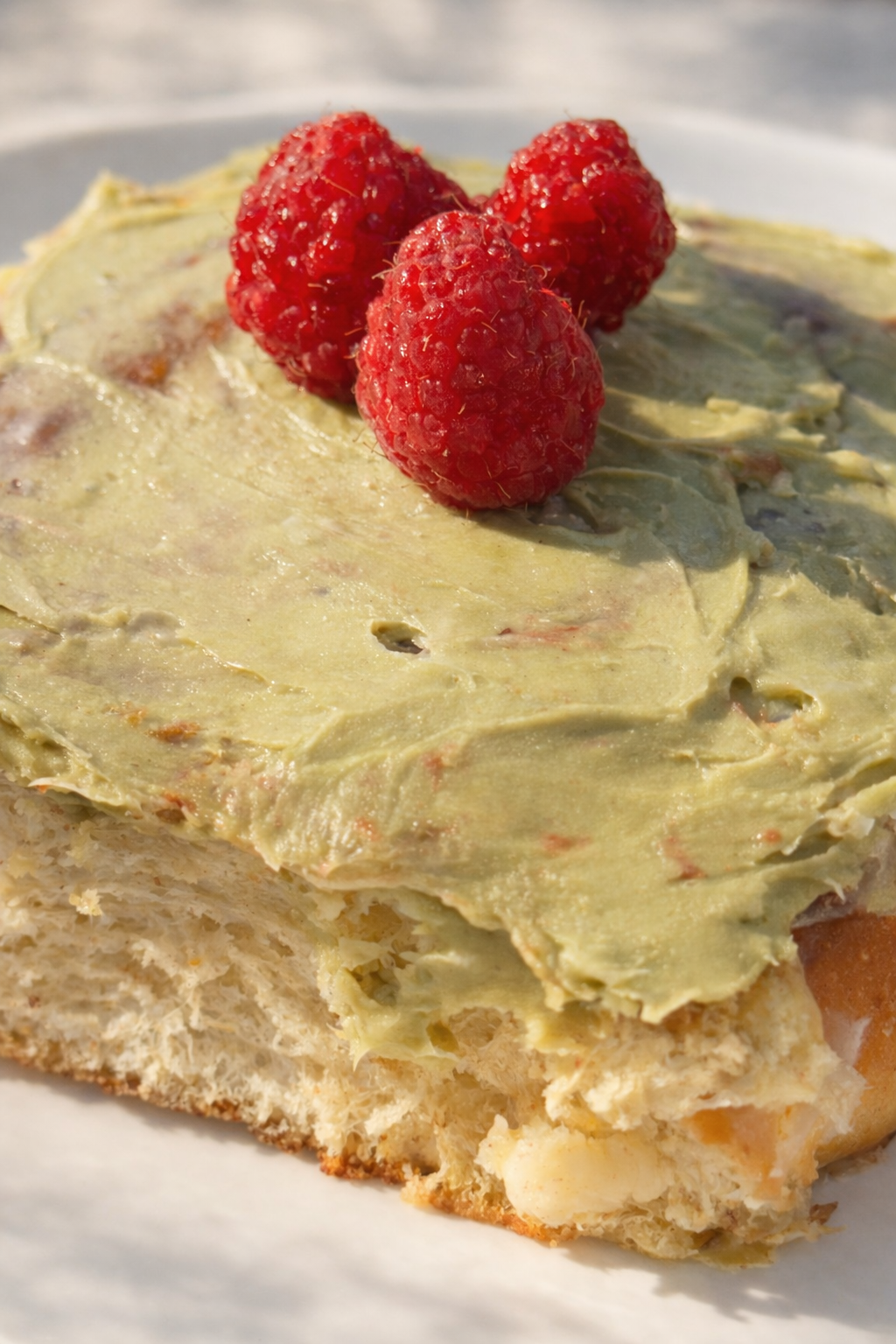 Matcha frosted cinnamon rolls with raspberries on a white plate